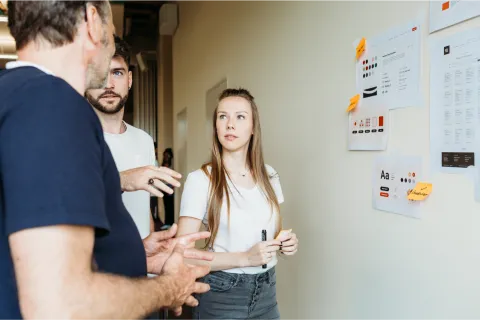Two men and a woman discussing ideas at a whiteboard