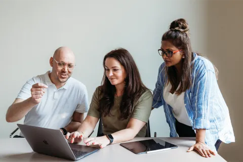 Three colleagues working together on a laptop at a table
