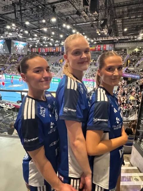 Three female handball players in blue uniforms in a sports arena