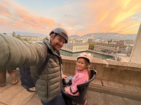 Father and daughter in helmets, smiling with a sunset over a cityscape