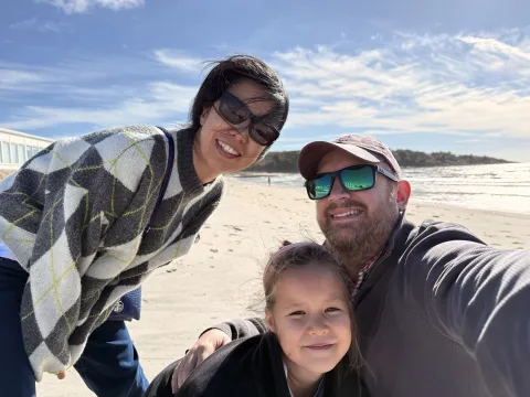 A family smiling together on the beach, with waves and blue sky
