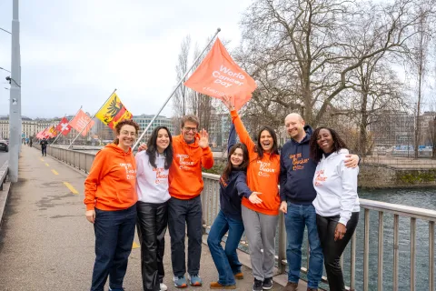 Seven people in orange and white clothing smiling and waving WCD flags