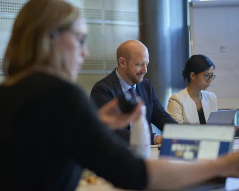 In a meeting, three professionals focus on laptops