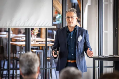 A speaker in a suit gestures while addressing an audience