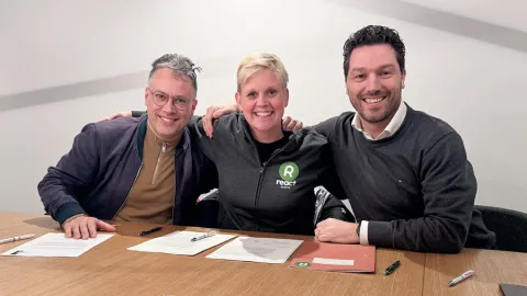 Three smiling people at a table with papers in front of them