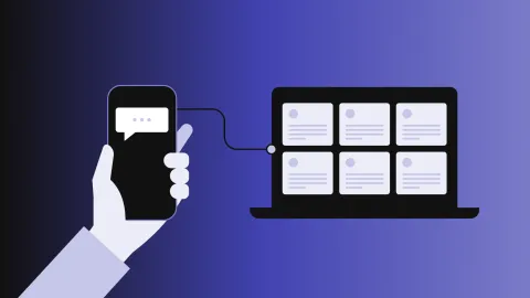 A hand holding a smartphone connected to a laptop with multiple screens